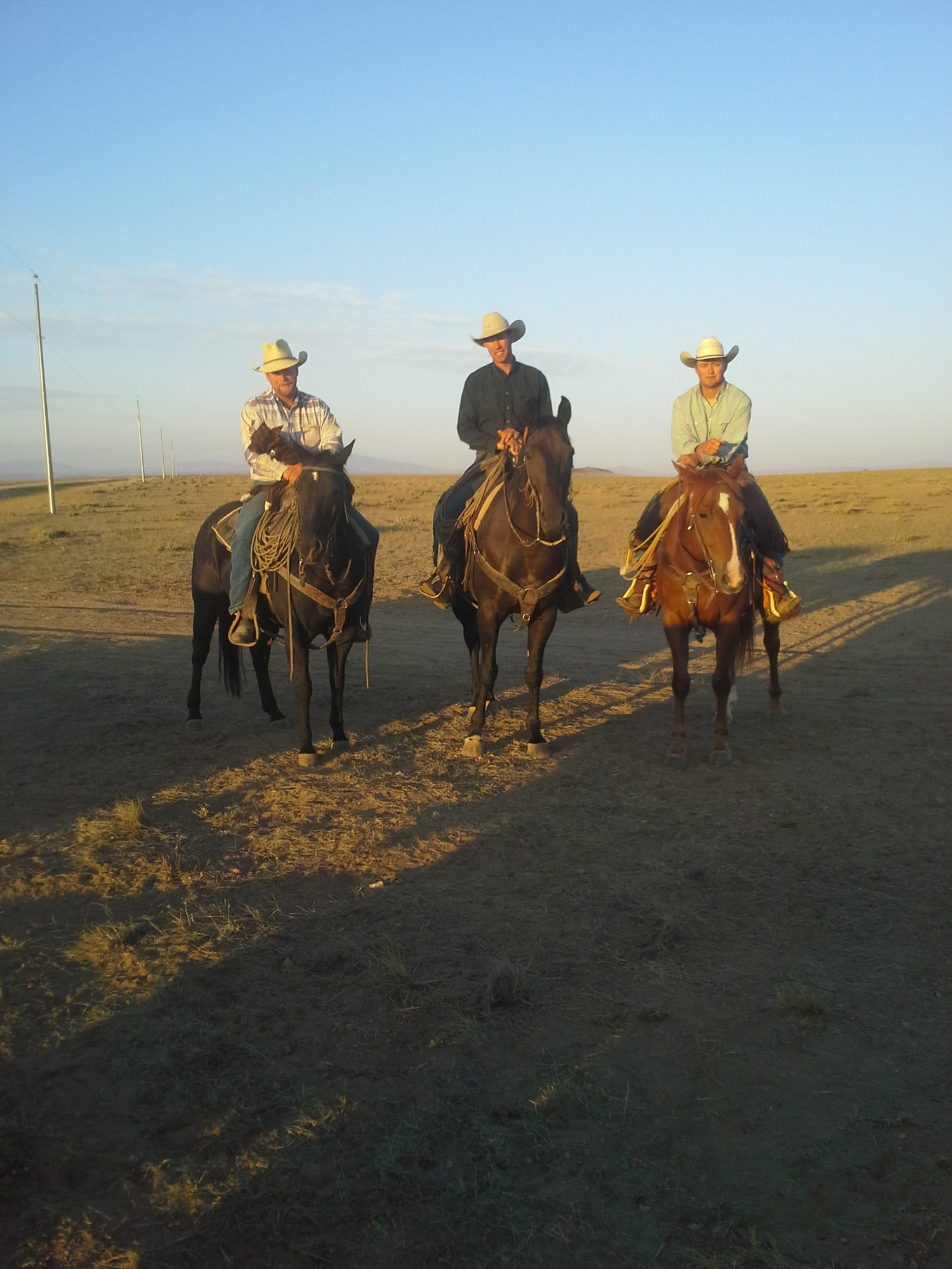 Three riders on horseback at the Askin ranch, long shadows across the grass in early morning light